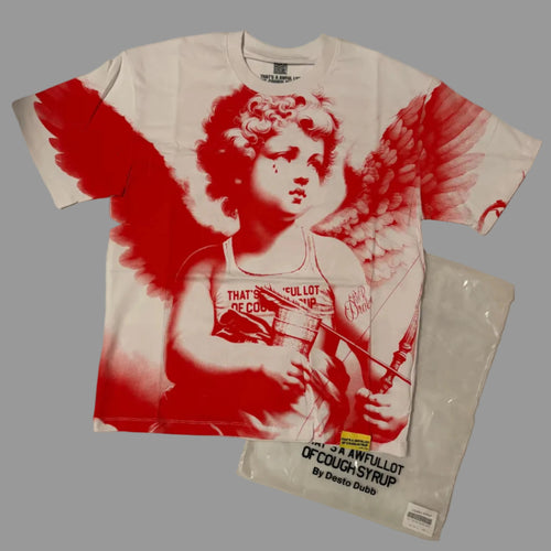 A white graphic t-shirt featuring a red and white print of a winged cherub holding a syringe, laid flat on a wrinkled white sheet next to a clear plastic bag with printed text.
