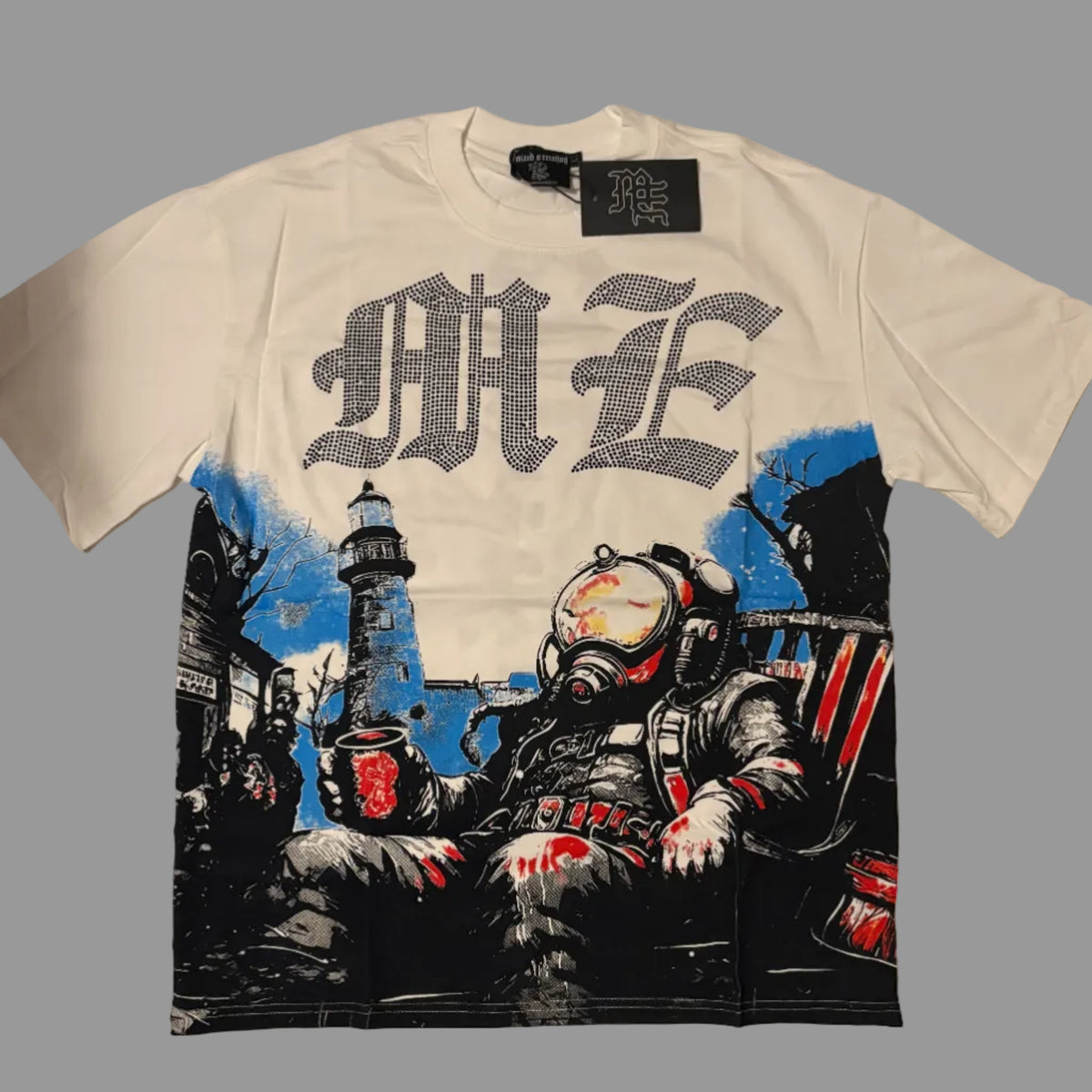 A white short-sleeve graphic t-shirt laid flat on a white fabric background. The shirt features a large black gothic-style 'ME' text across the chest and a detailed graphic print below showing a diver in a helmet next to a lighthouse, with red and blue accents.
